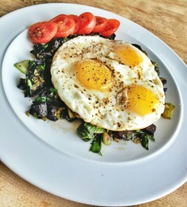 3 eggs cooked sunnyside up on a bed of sauteed beets and bok choy with tomato slices around the rim.